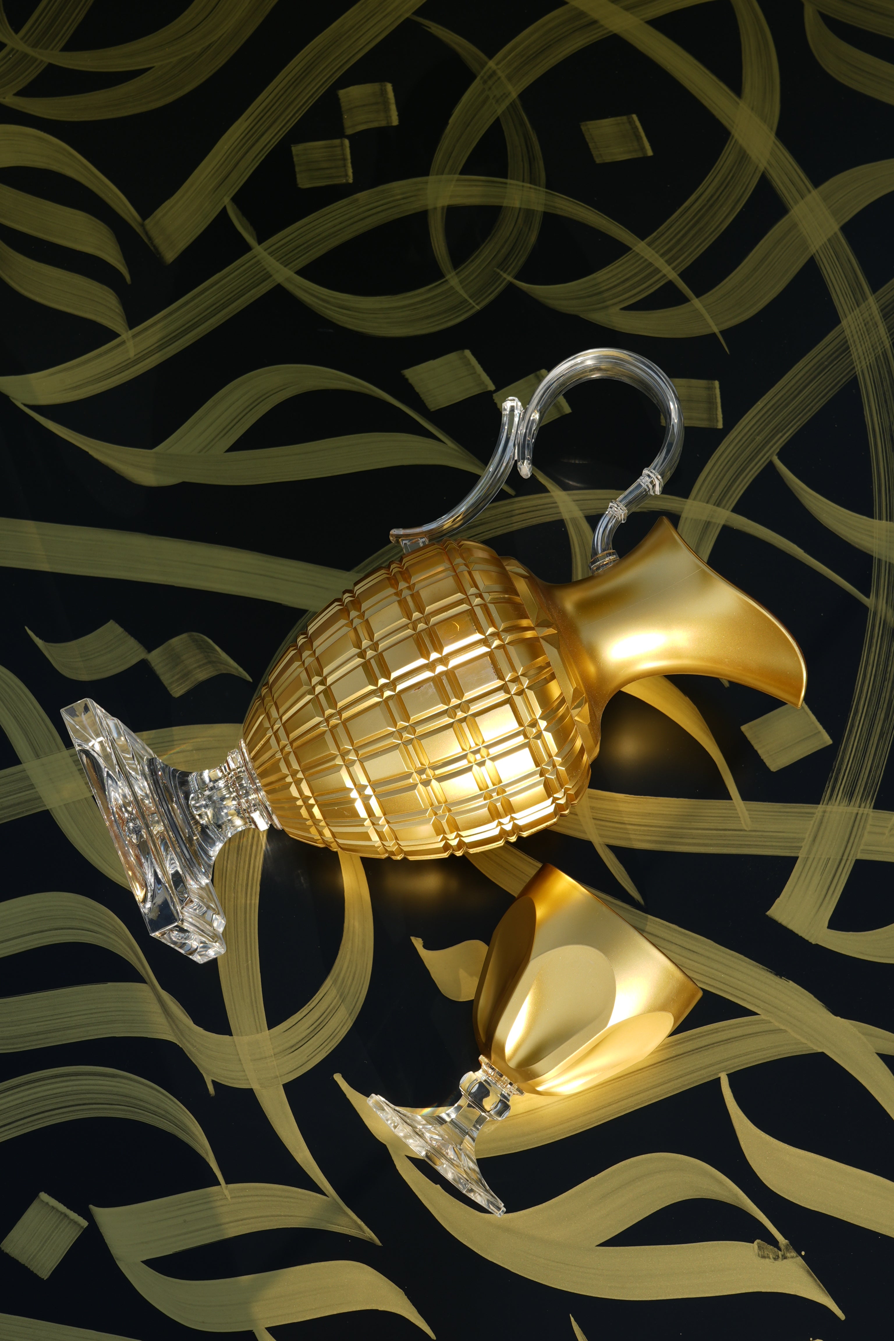 A gold Mario Luca Giusti pitcher poured toward a matching goblet on a black Arabic-calligraphy surface, set for an elegant qahwa welcome