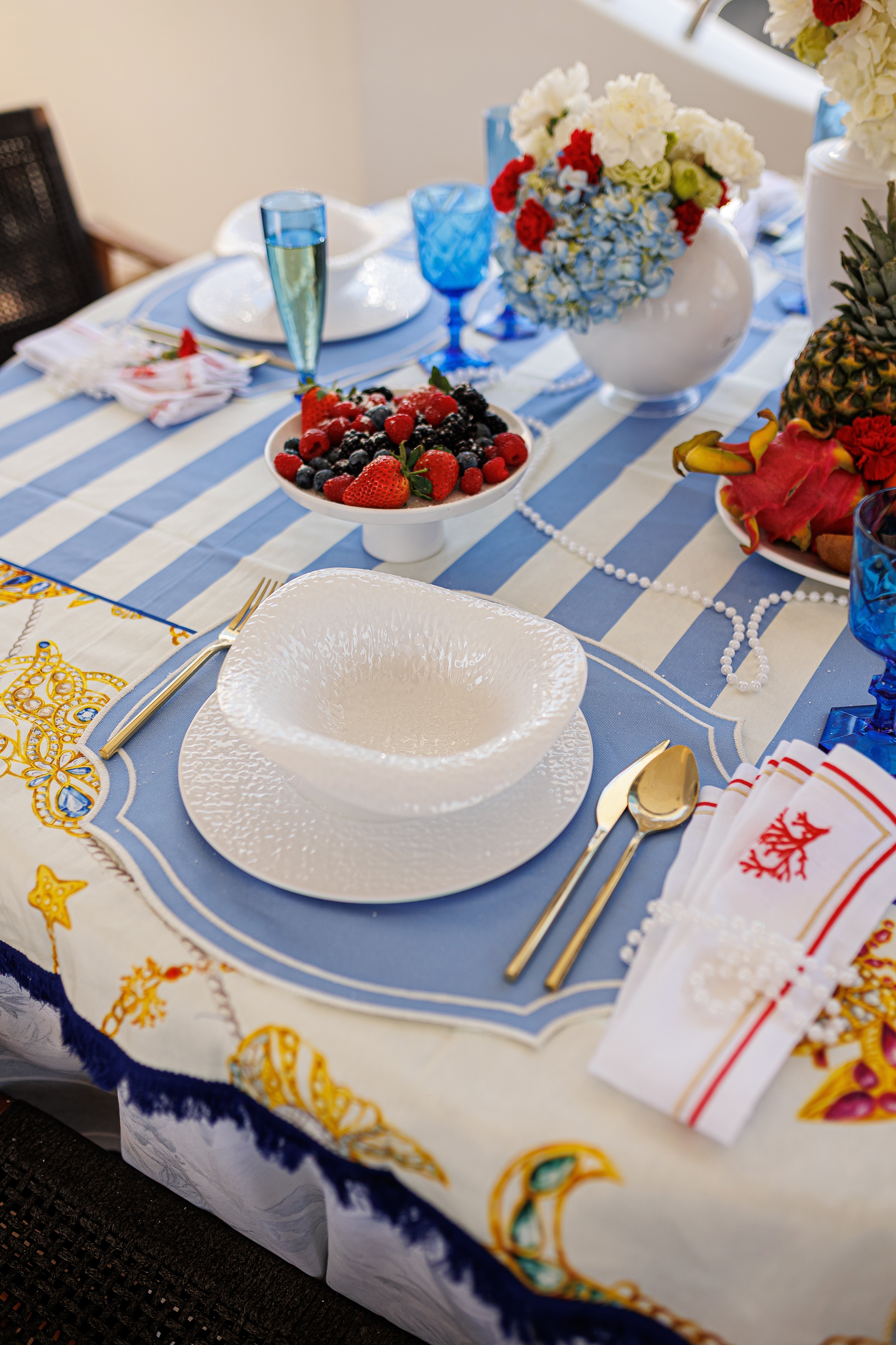 A coastal place setting pairing a white Baci Milano textured plate and bowl with a cobalt Mario Luca Giusti goblet on a blue-and-white striped table