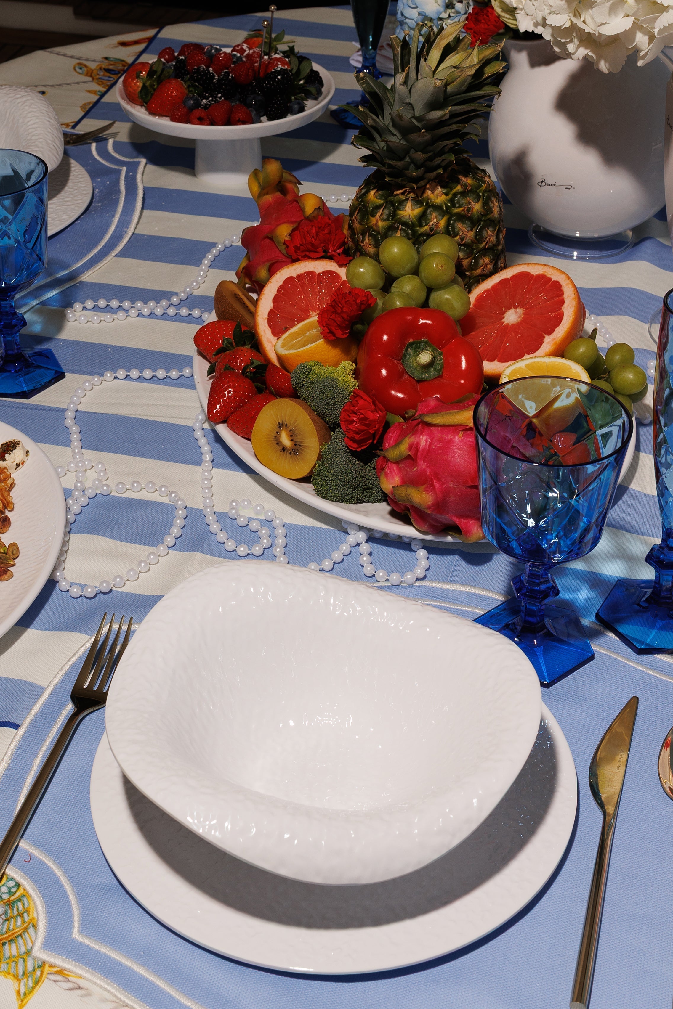 Bright Jeddah coastal table with blue-and-white striped linen, cobalt Italian glasses, white textured bowls and a vibrant Red Sea fruit centrepiece