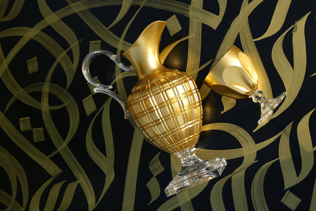 Gold Italian pitcher and goblet against dark Arabic calligraphy — a considered Gulf host gift