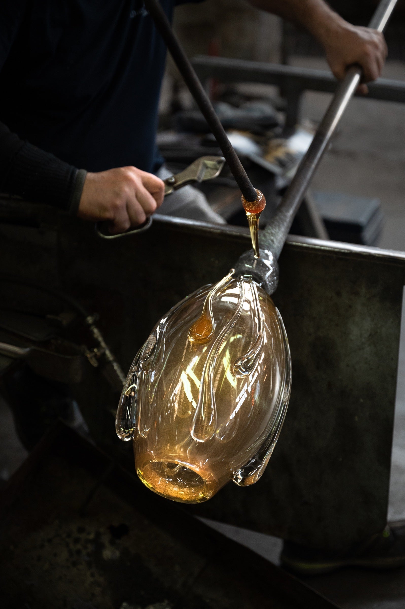 Glassblower shaping a molten amber vase with applied glass drops on the blowpipe in an Italian glass workshop