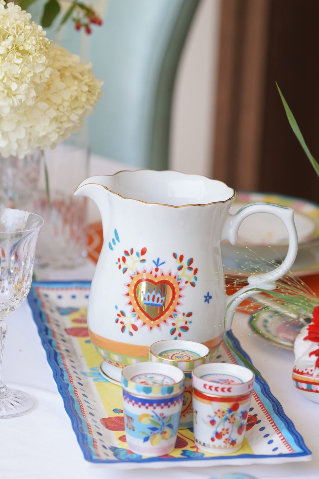 Mamma Mia porcelain pitcher with folk heart motif and espresso cups on a printed runner at a Tuscan villa table