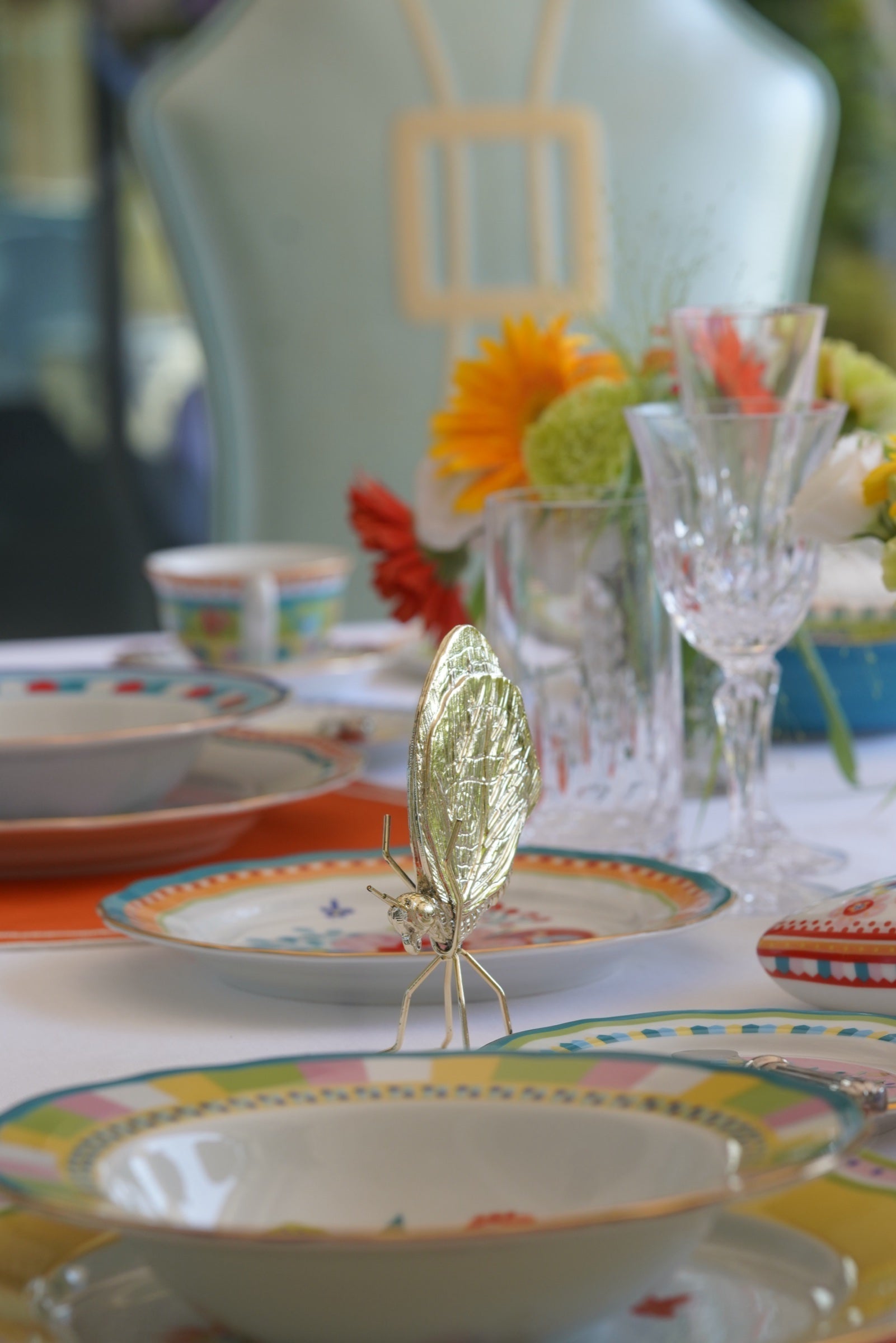 Festive table detail with patterned Italian plates, crystal stemware and a silver insect place ornament