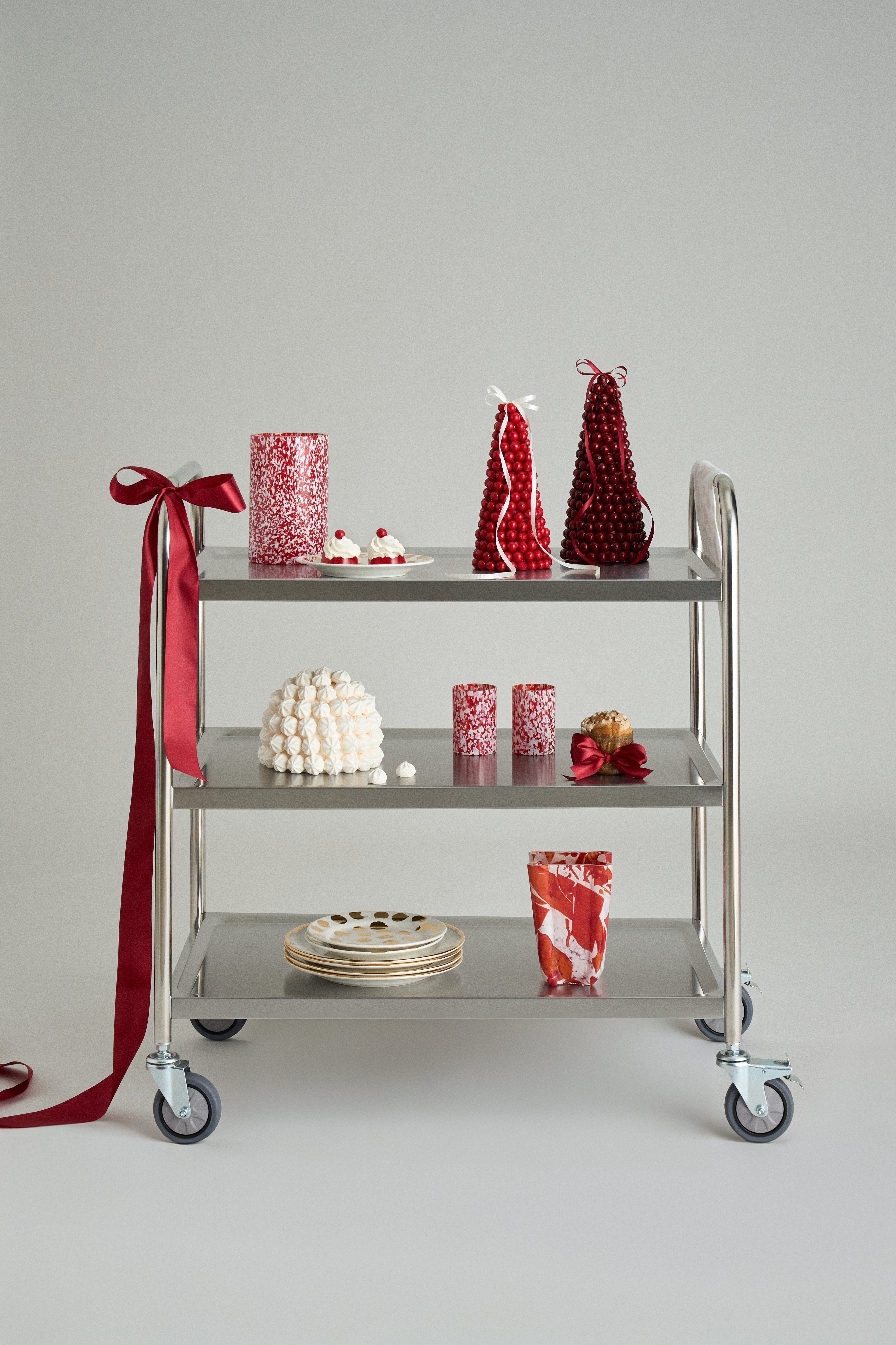 Stories of Italy serving cart styled with festive red Murano vessels, white textured vase and a draped gift ribbon