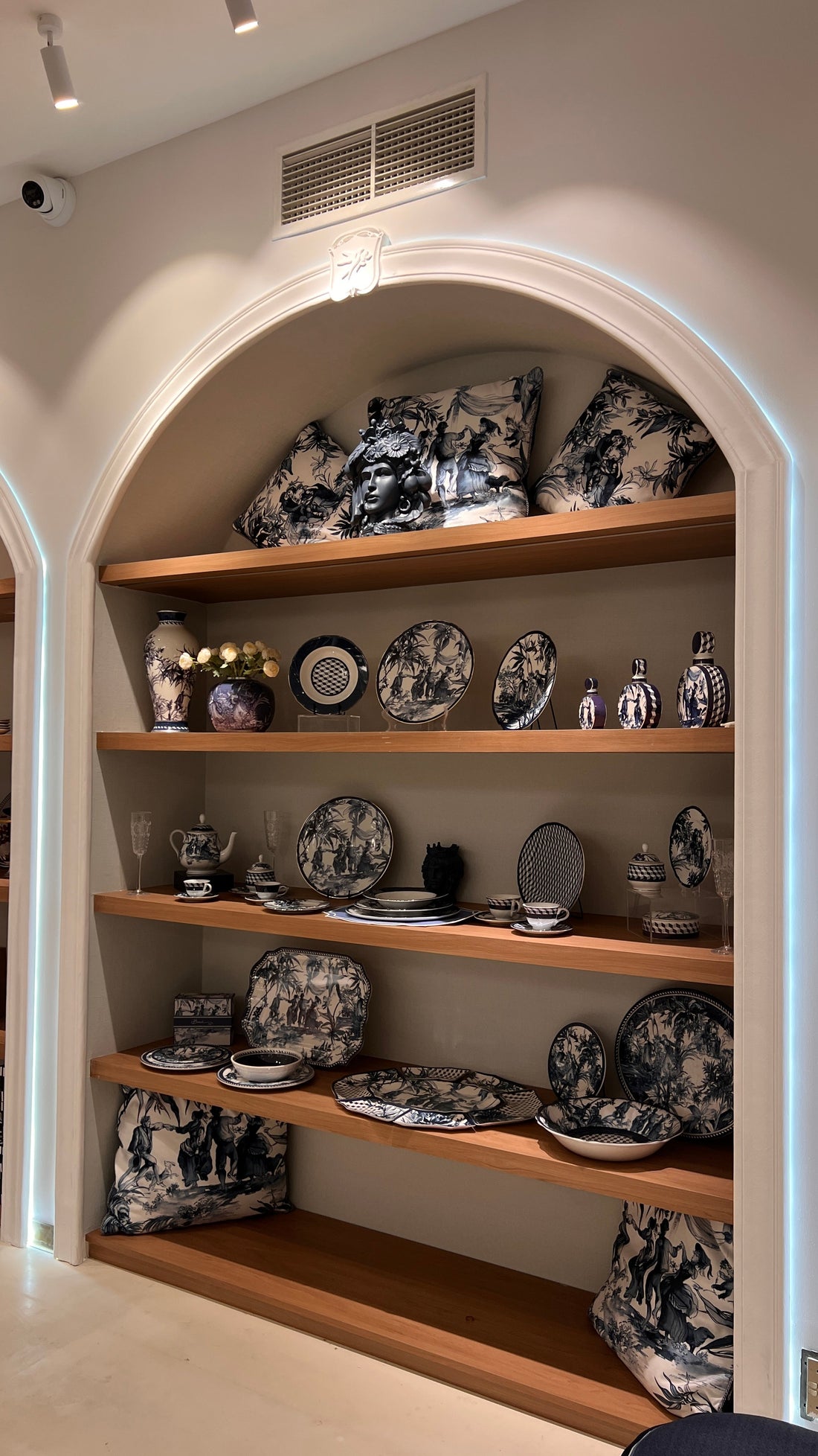 A blue-and-white Italian toile display on warm wood shelves — patterned plates, a serving tray, teapot and vases arranged for a Gulf welcome