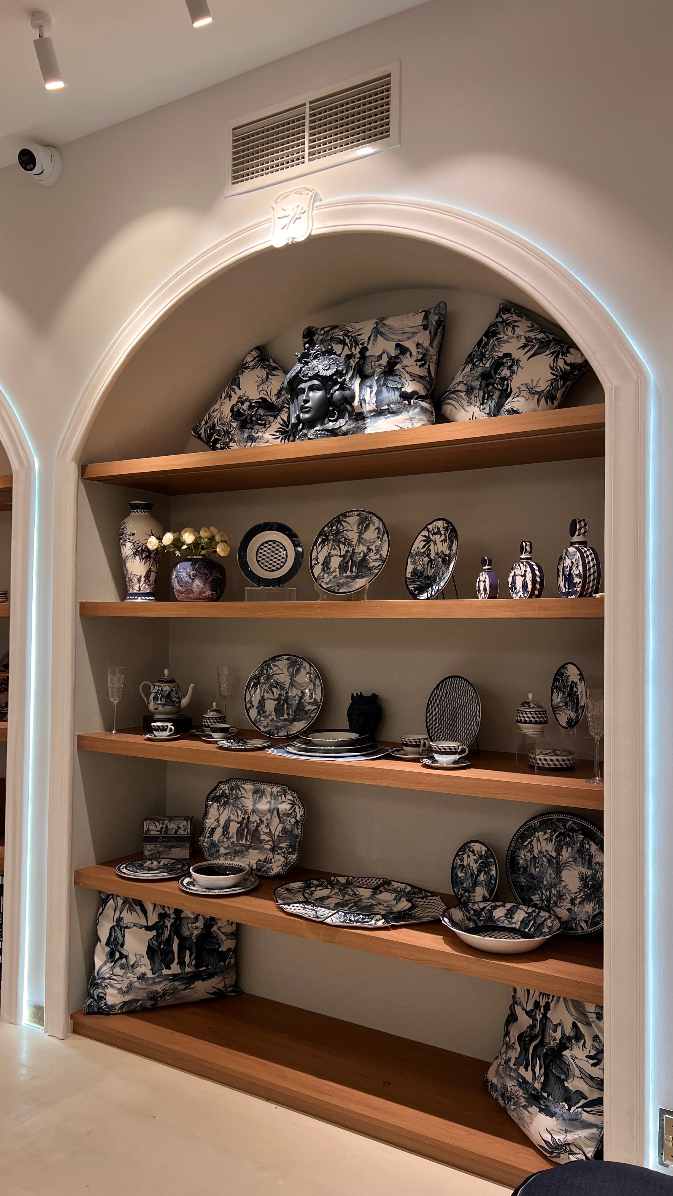 A blue-and-white Italian toile display on warm wood shelves — patterned plates, a serving tray, teapot and vases arranged for a Gulf welcome