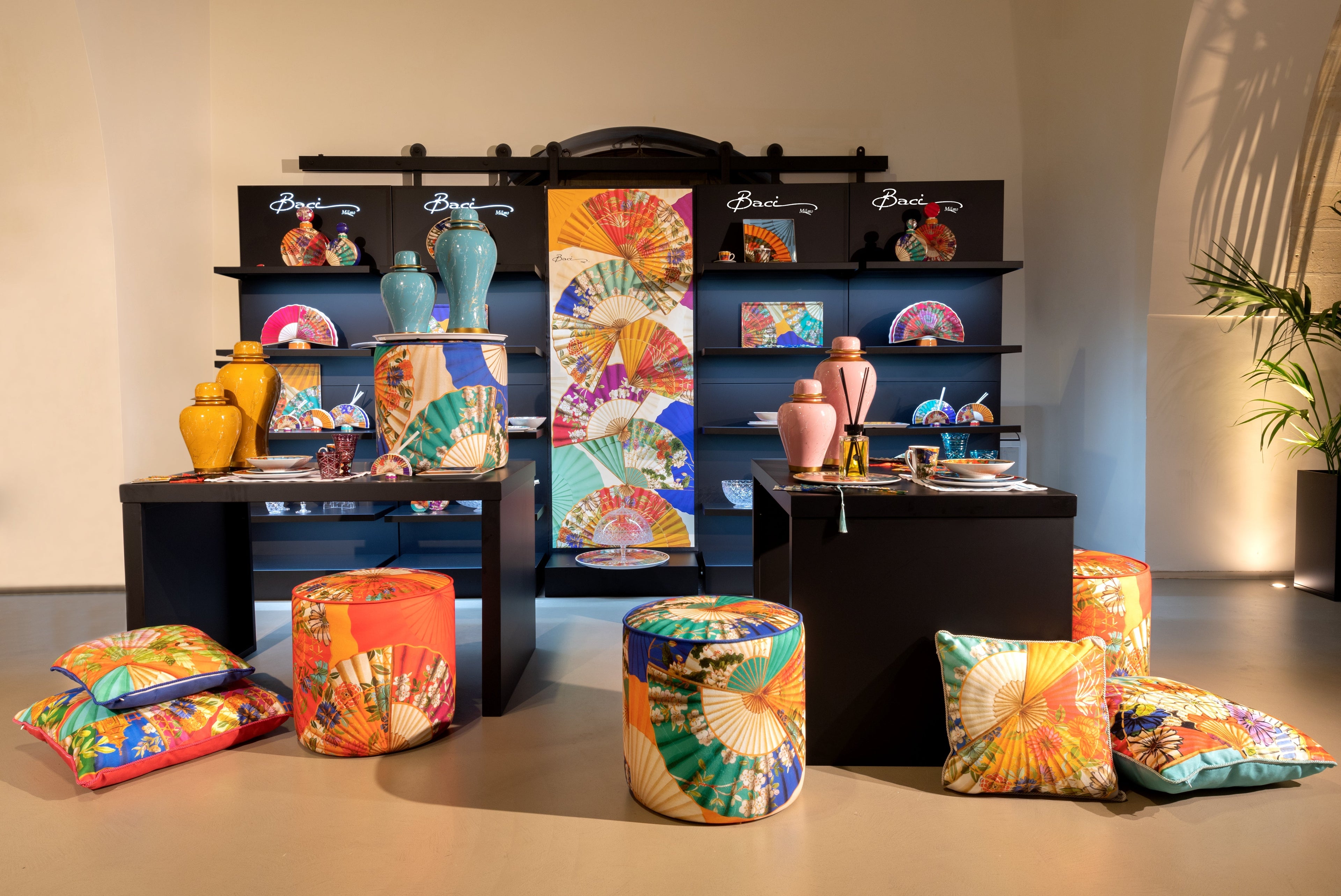 Ventagi collection display — decor cushions and poufs with colourful fan prints, ceramic vases and trays